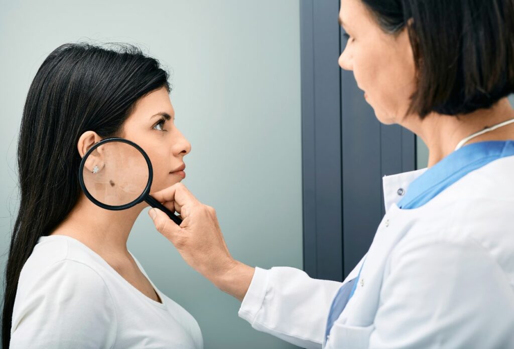 Dermatóloga observa el lunar de una paciente joven a través de una lupa.